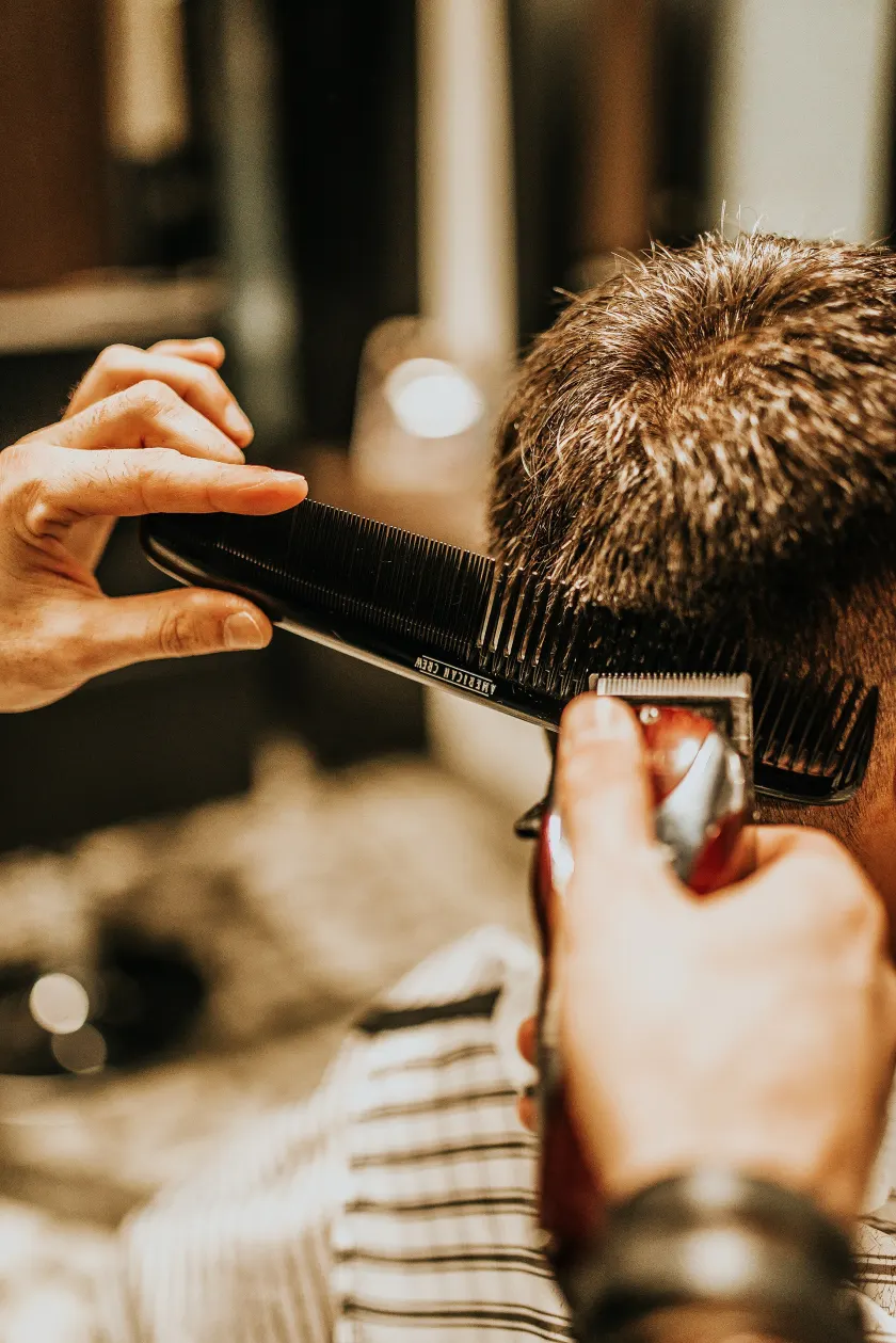 A barber cutting a customer's hair, both seen from behind in a barber shop