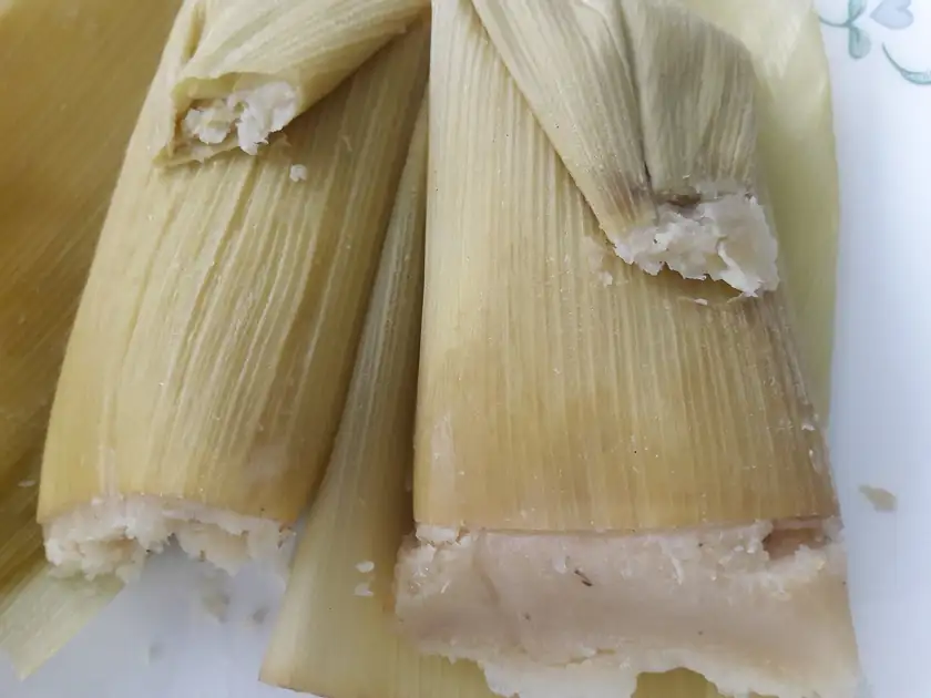 Several tamales in corn husks arranged on a metal tray