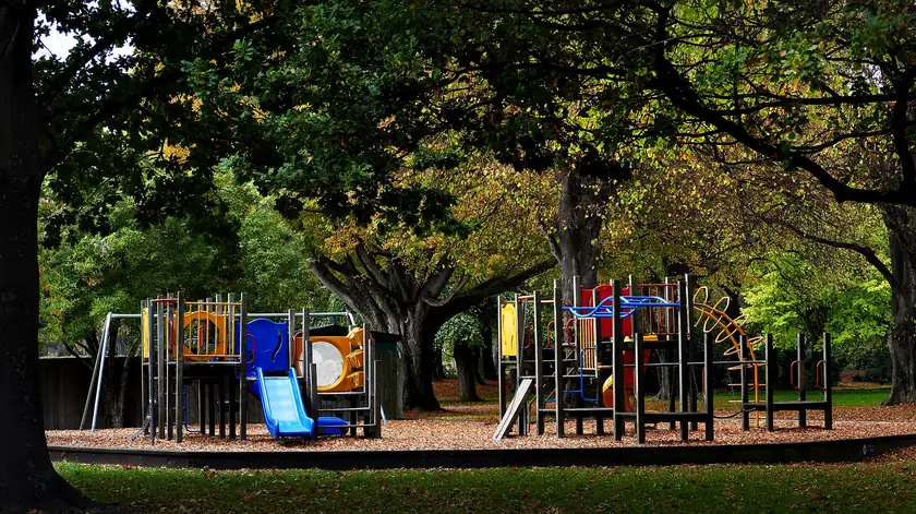 An empty wooden playground structure on a lawn with no children nearby