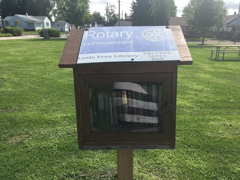 A small wooden book-sharing box on a post beside a sidewalk