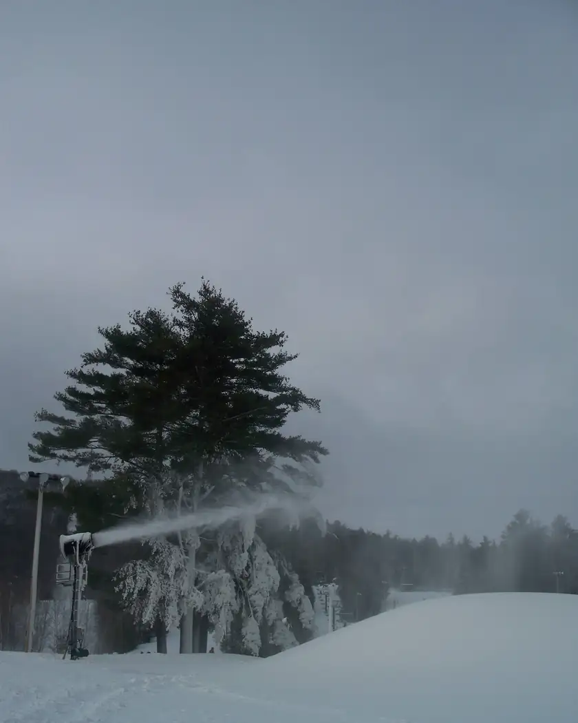 Snow guns blowing a plume of machine-made snow across a ski slope