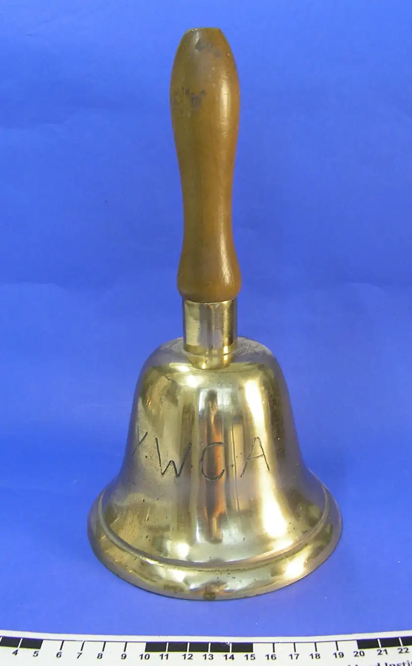 A small brass handbell hanging against a plain background