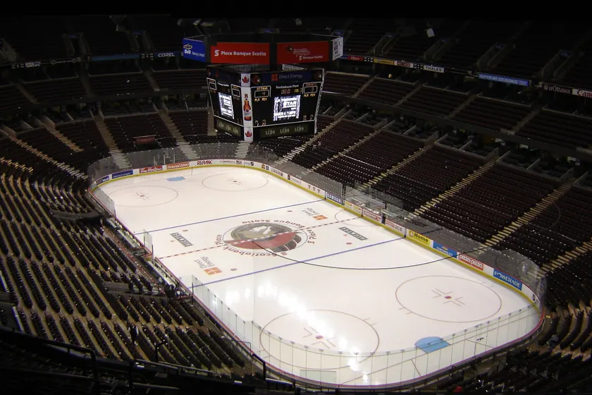 An empty indoor hockey arena with rows of red seats above a bare sheet of ice
