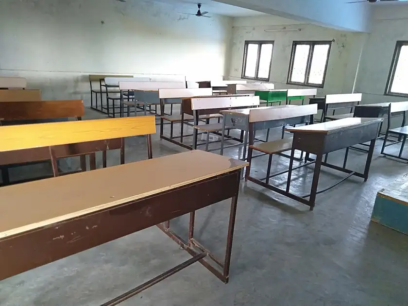 An empty classroom with rows of desks and a green chalkboard
