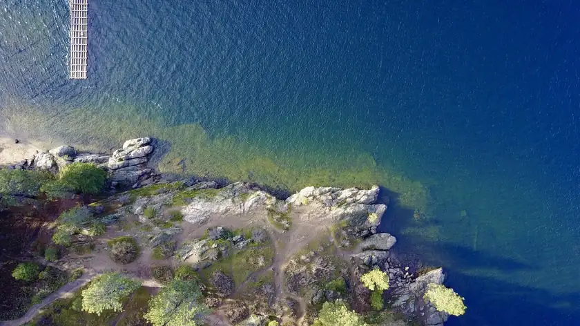 Aerial view of a rocky, tree-dotted shoreline meeting deep blue water on Lake Coeur d'Alene