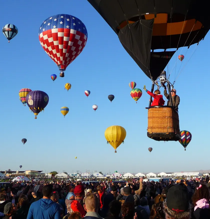 Many hot air balloons lifting off a field at once, with spectators in the foreground