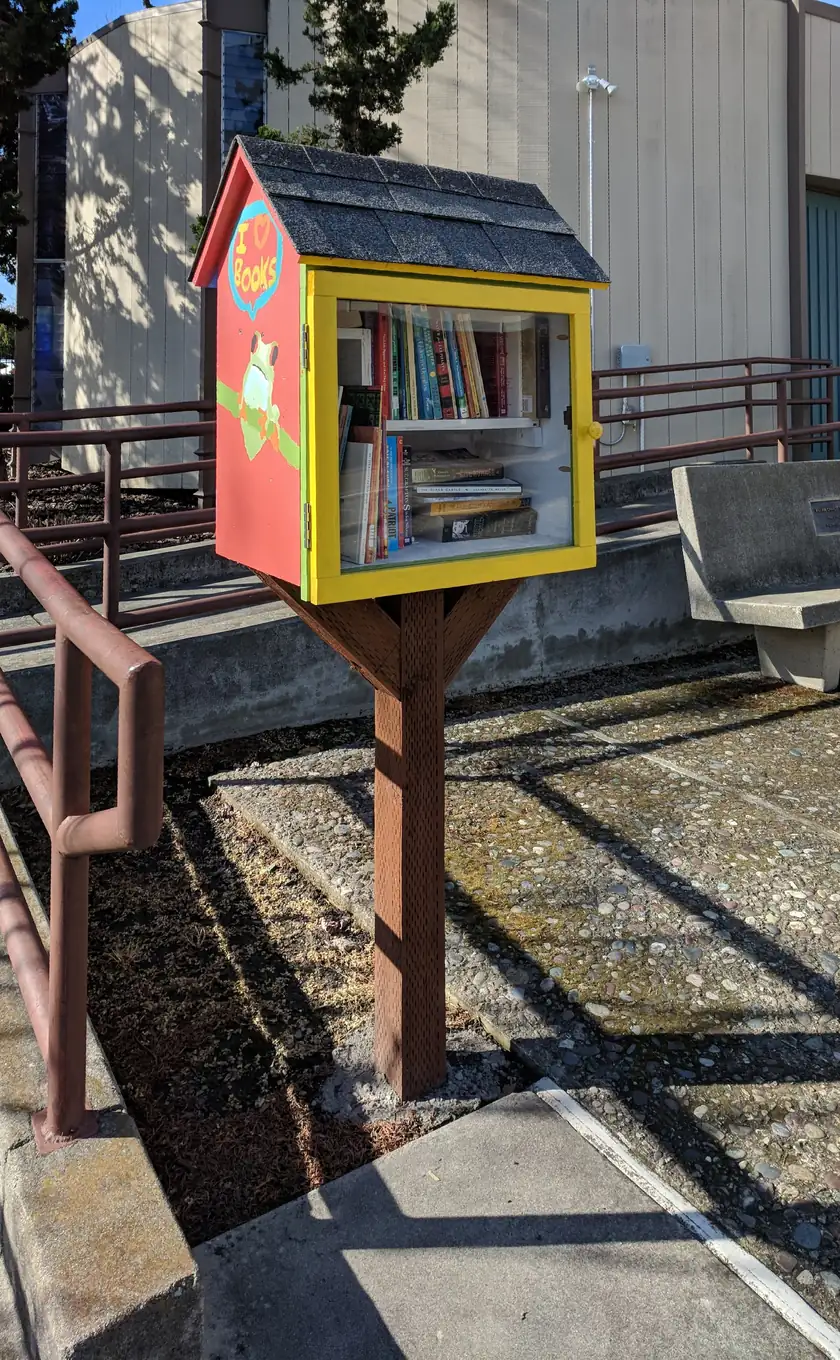 A wooden little free library box with glass doors on a residential sidewalk