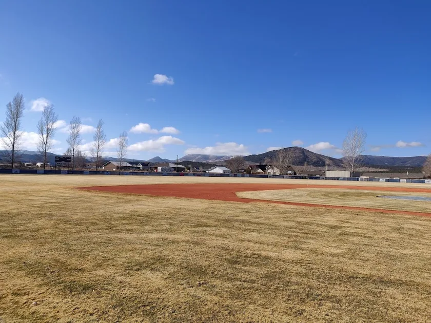 An empty dirt and grass baseball field under a blue sky with mountains behind