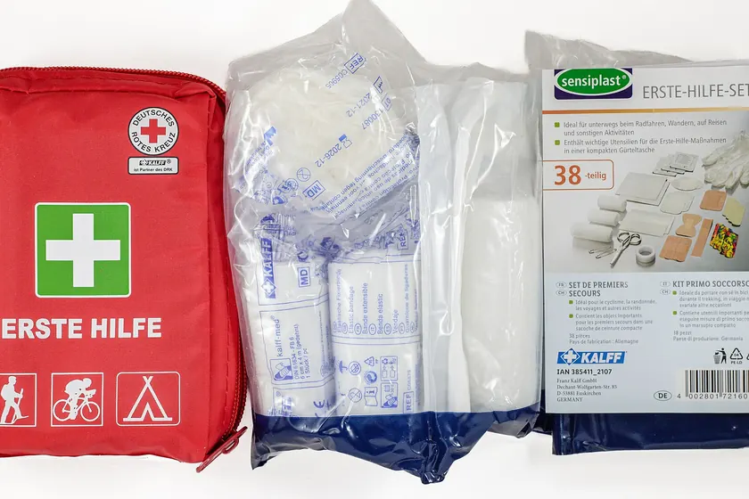 An open red soft-sided first aid kit with bandages and labeled supply pockets