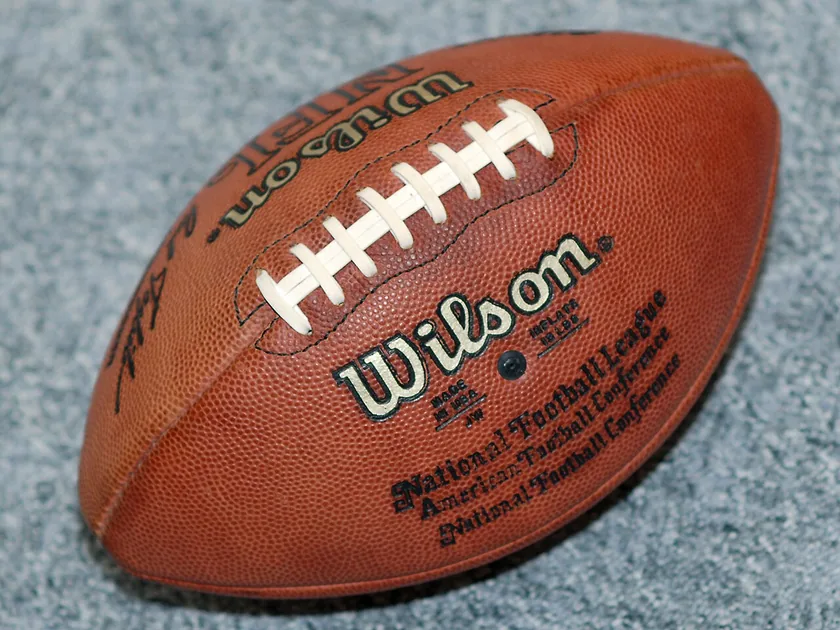 A brown Wilson American football with white laces and stripes lying on pavement