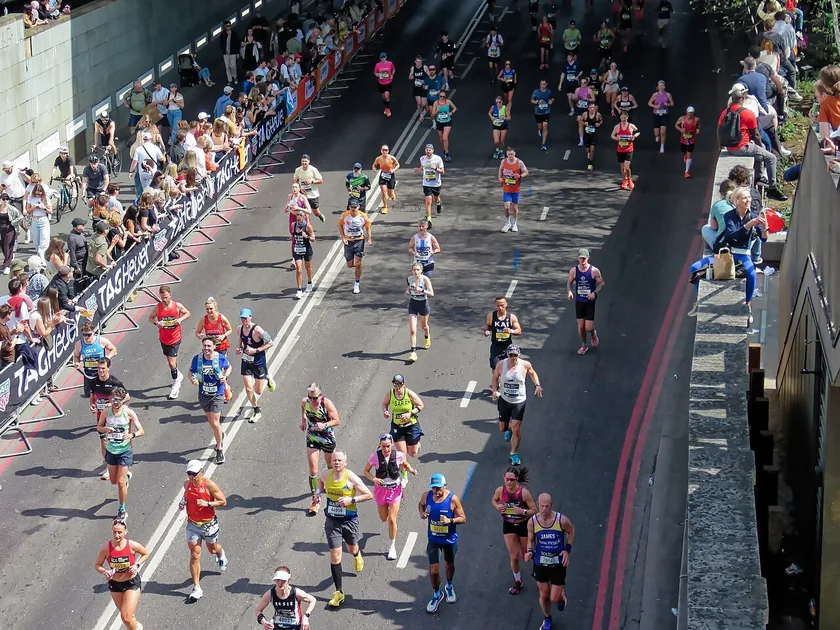 A dense pack of marathon runners seen from behind on a city street, with spectators along the curb