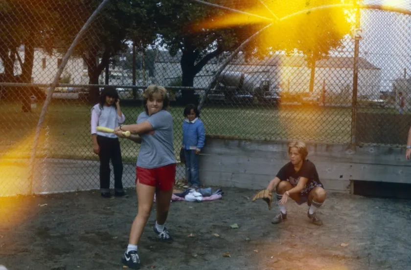 Children playing ball on a grassy field, one of them holding a bat