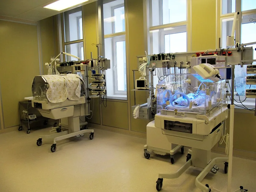 Medical staff in masks and hair covers beside an incubator in a neonatal intensive care unit
