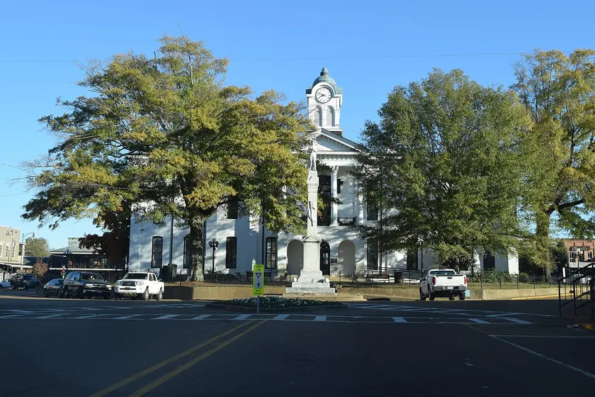 A pale stone courthouse with a clock tower, columns, and a green lawn