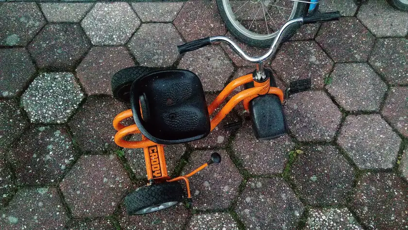 A children's bicycle and a small tricycle parked on pavement, with no riders