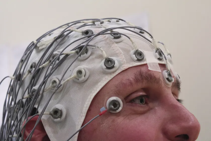 A person seen from behind wearing a blue cap fitted with EEG sensors and wires