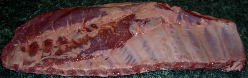Raw pork spare ribs laid in overlapping rows on a metal tray