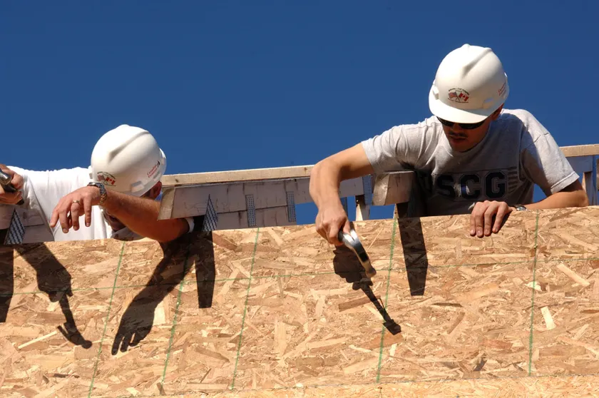 Volunteers in work gloves repairing the wooden siding of a house