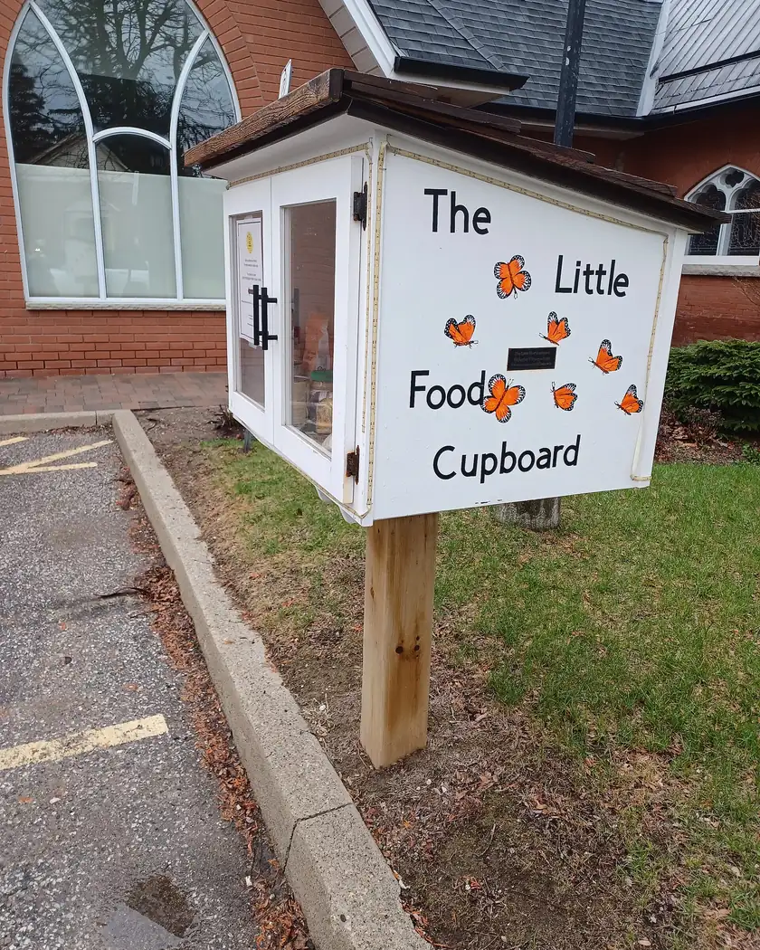 A small wooden food cupboard with glass doors stocked with canned goods