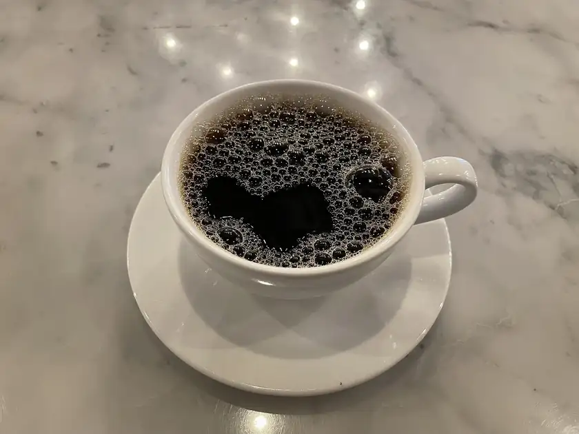 A white cup of coffee on a metal cafe table, with no people in the frame
