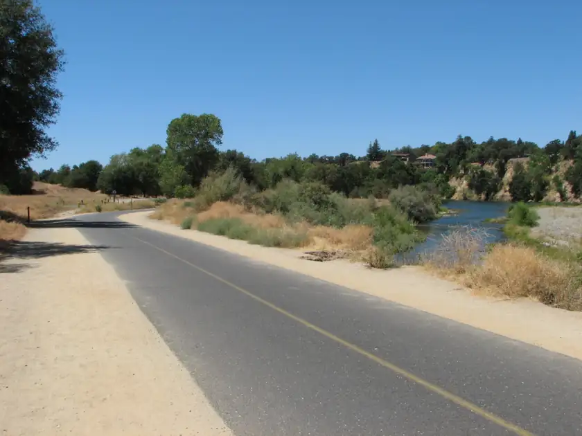 A paved riverside bike trail through trees, with no people in the frame