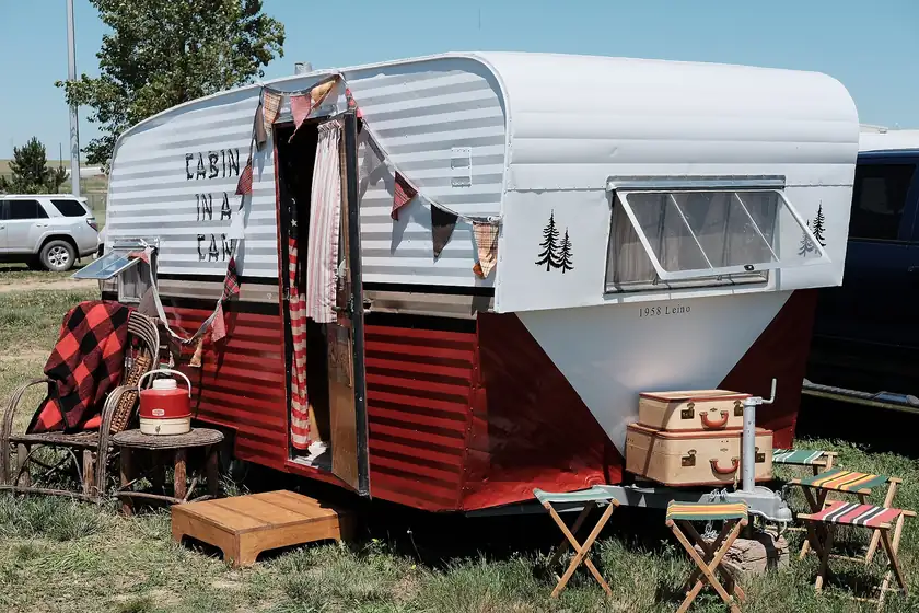 A white 1958 Shasta travel trailer parked on pavement at a camper rally